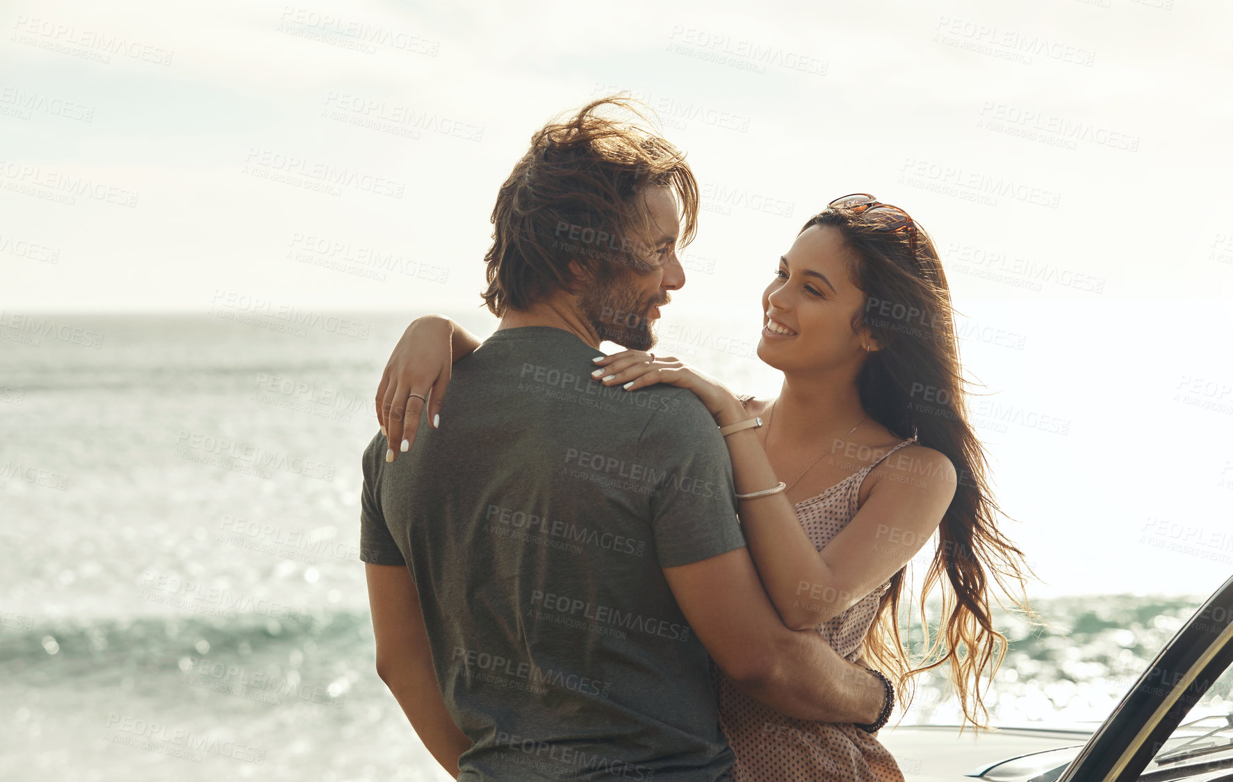 Buy stock photo Cropped shot of an affectionate young couple holding each other and standing together on the beach during a road trip