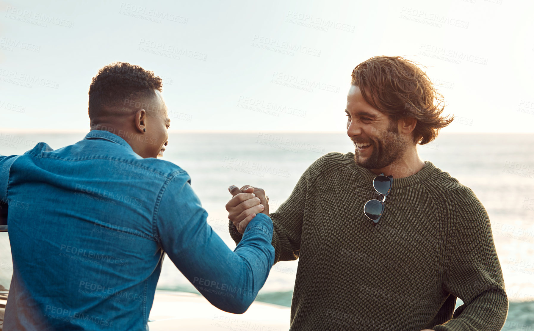 Buy stock photo Cropped shot of two handsome young men greeting each other at the beach during a road trip