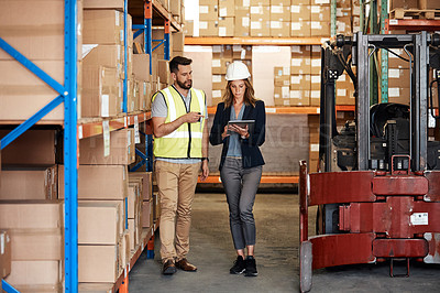 Buy stock photo Full length shot of an attractive young businesswoman walking through a warehouse with a male worker