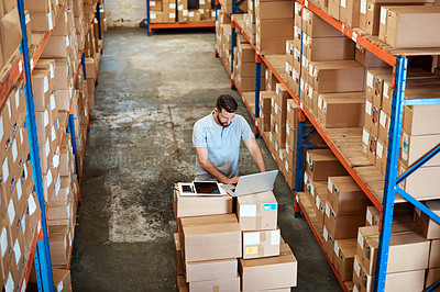 Buy stock photo High angle shot of a handsome young male warehouse worker working on a laptop