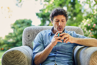 Buy stock photo Shot of a handsome mature man relaxing in a chair and drinking coffee in his backyard