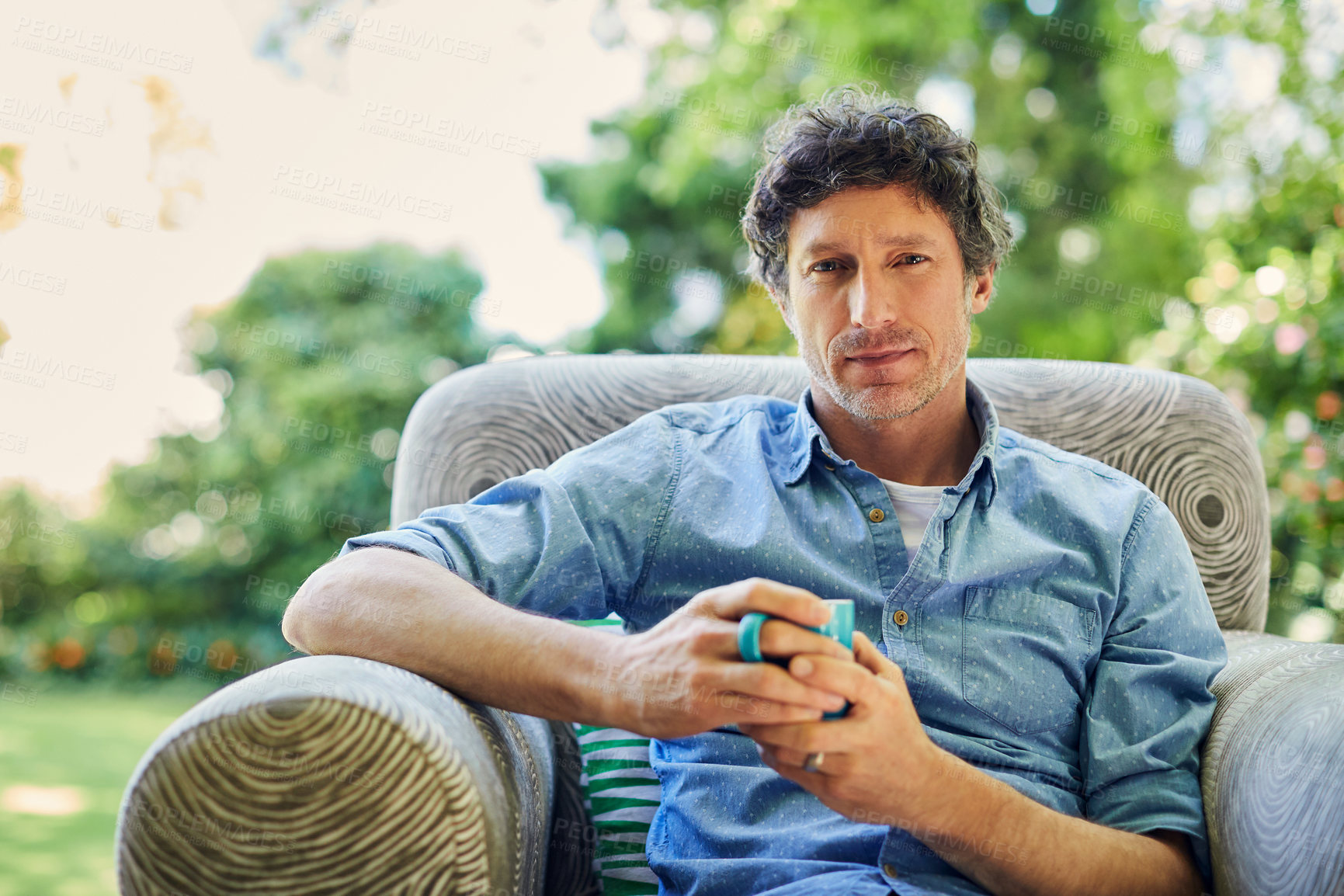 Buy stock photo Shot of a handsome mature man relaxing in a chair and drinking coffee in his backyard