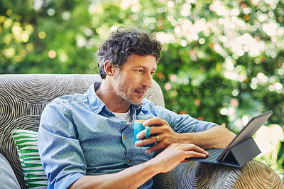 Buy stock photo Shot of a mature man relaxing in a chair while using a digital tablet and drinking coffee in his backyard
