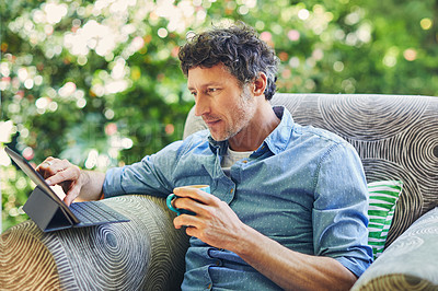 Buy stock photo Shot of a mature man relaxing in a chair while using a digital tablet and drinking coffee in his backyard