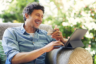Buy stock photo Shot of a mature man relaxing in a chair while using a digital tablet and credit card in his backyard