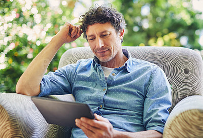 Buy stock photo Shot of a mature man relaxing in a chair and using a digital tablet in his backyard