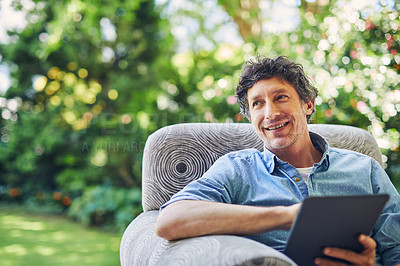 Buy stock photo Shot of a mature man relaxing in a chair and using a digital tablet in his backyard