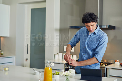 Buy stock photo Shot of a mature man using a digital tablet while making coffee at home in the morning.