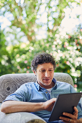 Buy stock photo Shot of a mature man relaxing in a chair and using a digital tablet in his backyard