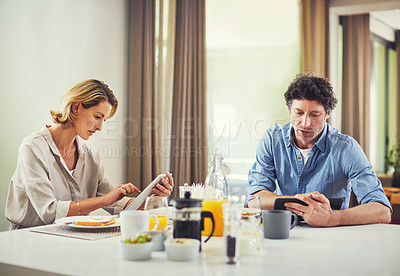 Buy stock photo Shot of a mature couple using digital tablets while having breakfast at home