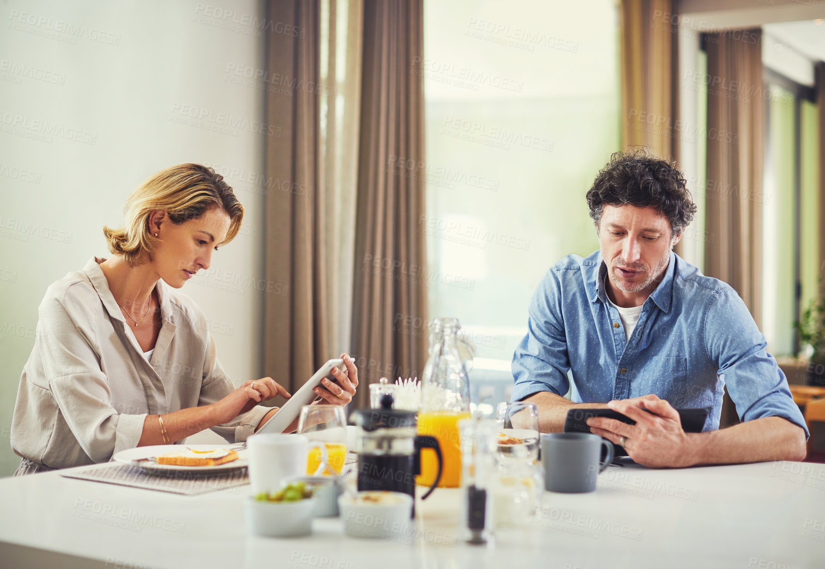 Buy stock photo Shot of a mature couple using digital tablets while having breakfast at home