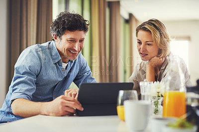 Buy stock photo Shot of a mature couple using a digital tablet while having breakfast at home
