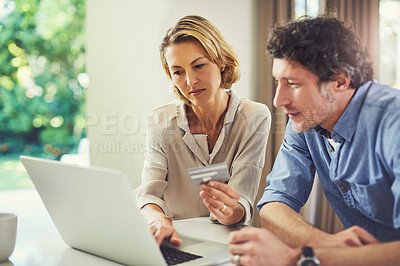 Buy stock photo Shot of a mature couple using a credit card while going over their finances at home
