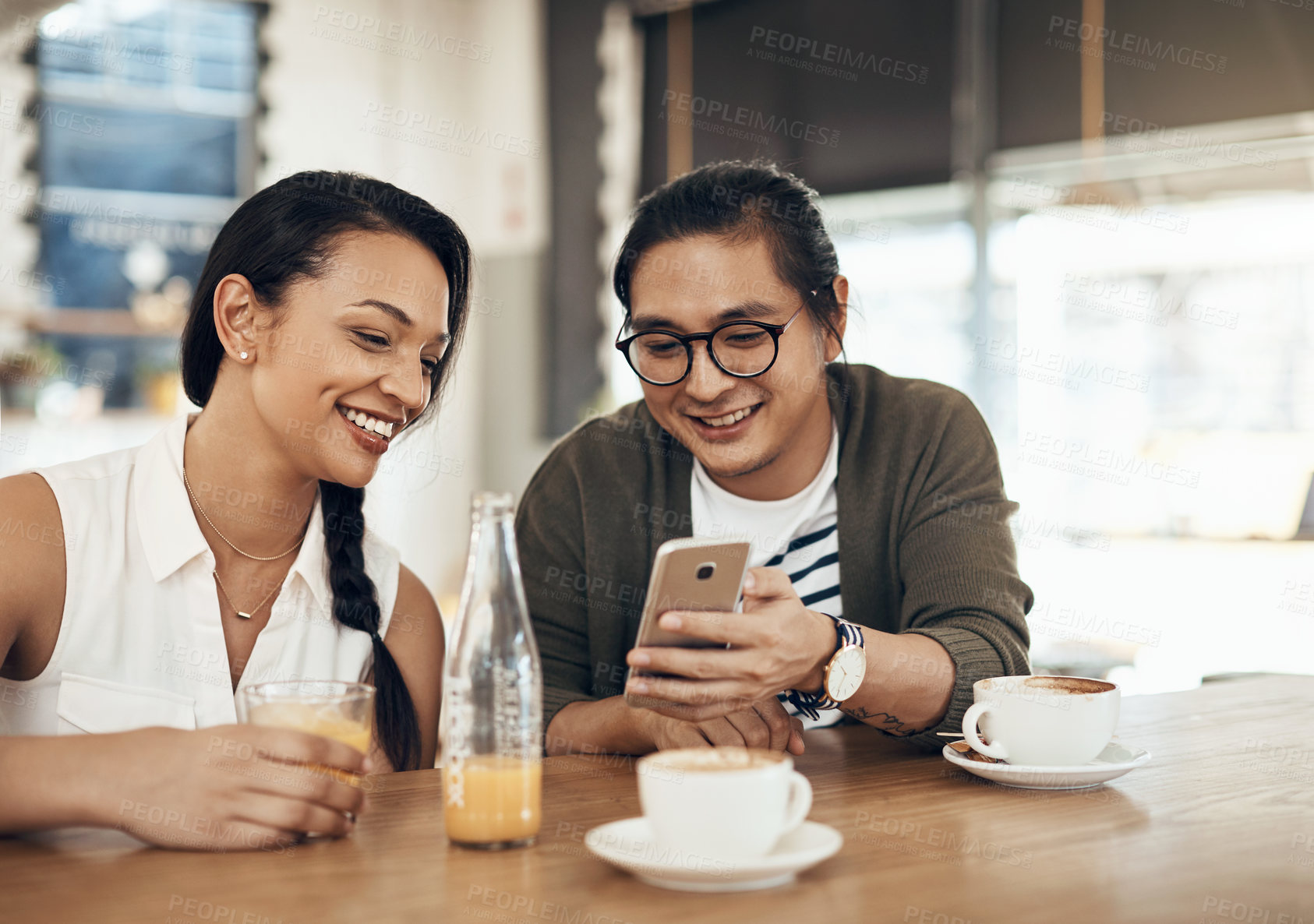 Buy stock photo Cropped shot of a handsome young man sitting with a female friend and using his cellphone in a cafe