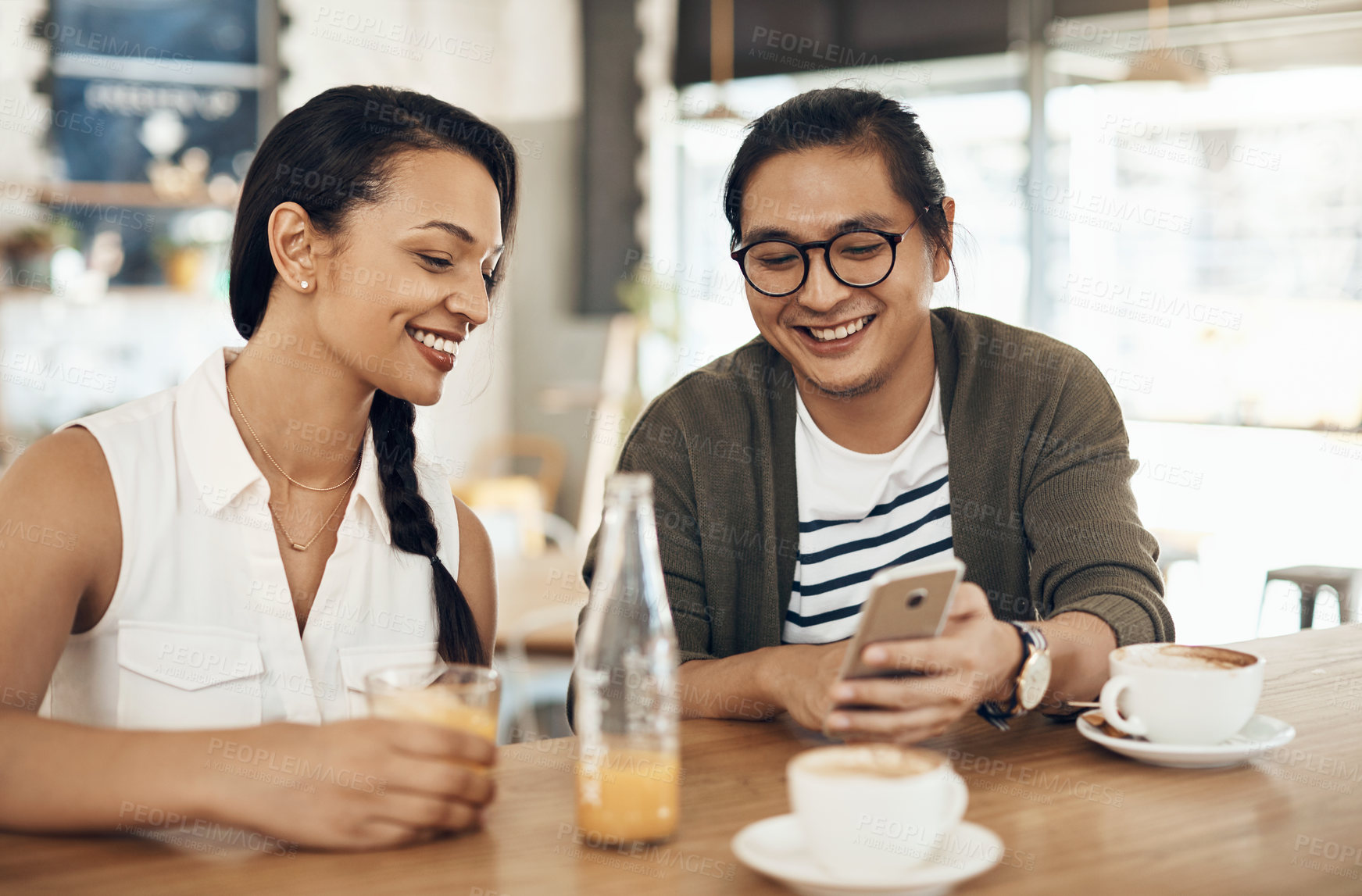 Buy stock photo Cropped shot of a handsome young man sitting with a female friend and using his cellphone in a cafe