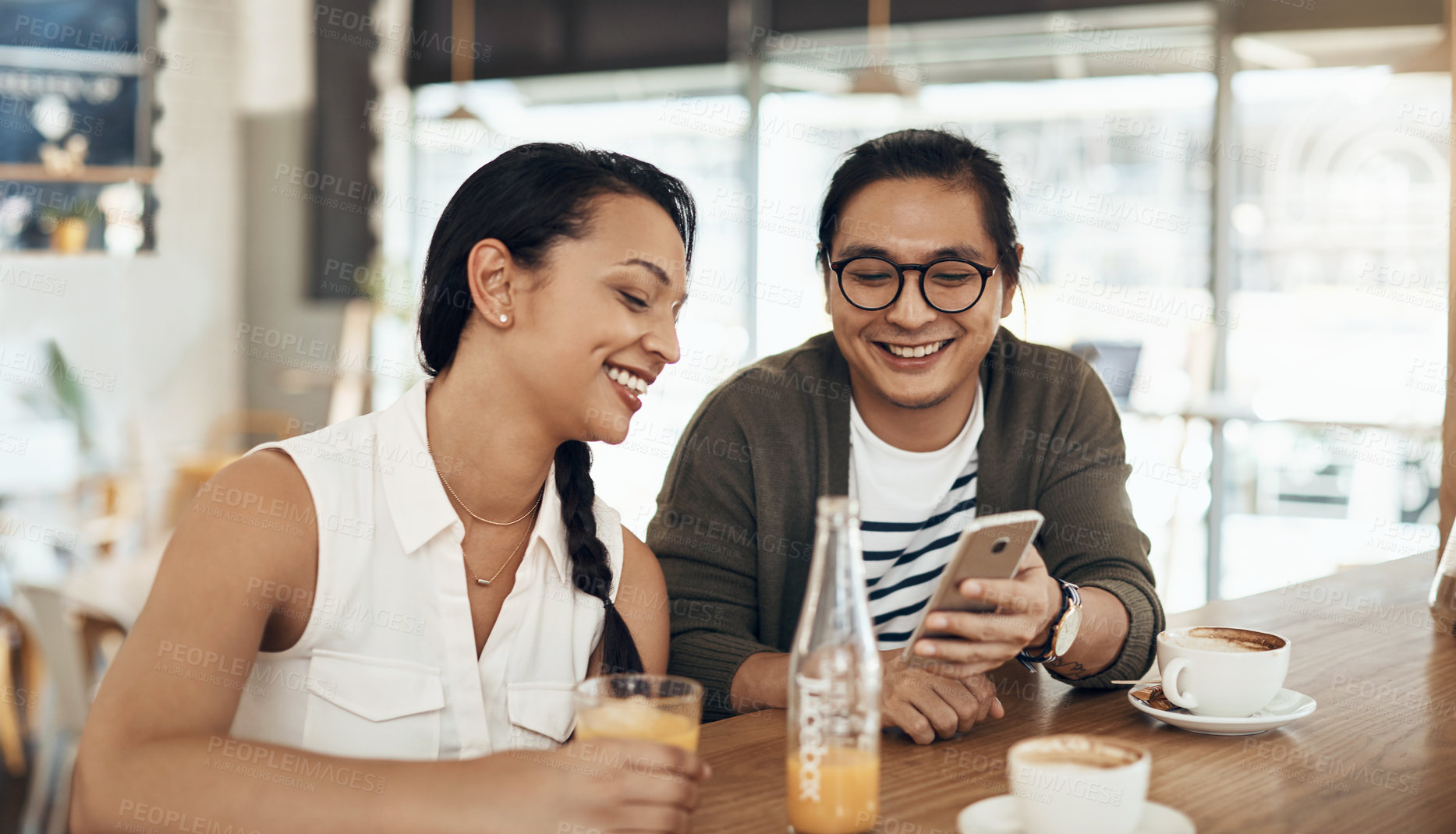 Buy stock photo Cropped shot of a handsome young man sitting with a female friend and using his cellphone in a cafe