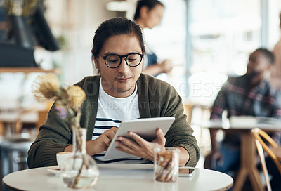 Buy stock photo Cropped shot of a handsome young businessman sitting on his own in a cafe and working on his tablet