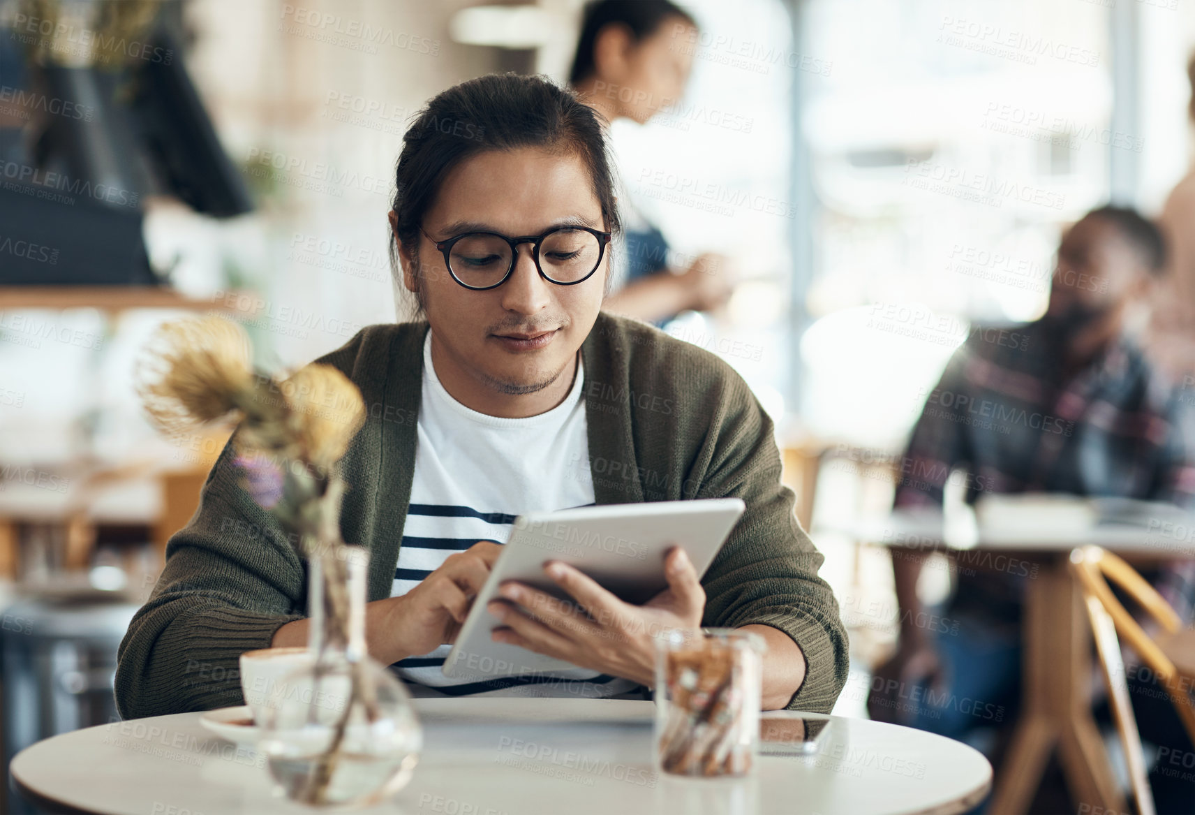 Buy stock photo Cropped shot of a handsome young businessman sitting on his own in a cafe and working on his tablet
