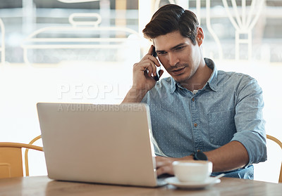 Buy stock photo Cropped shot of a handsome young businessman sitting and talking on his cellphone while using his laptop in a cafe