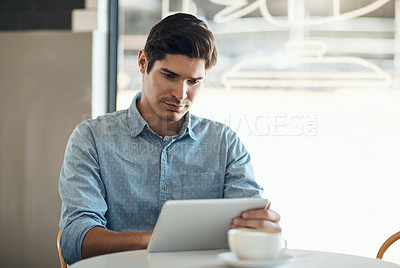 Buy stock photo Cropped shot of a handsome young businessman sitting on his own in a cafe and working on his tablet