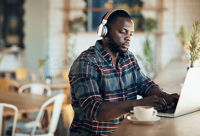 Buy stock photo Cropped shot of a handsome young businessman wearing headphones to listen to music and using his computer in a cafe