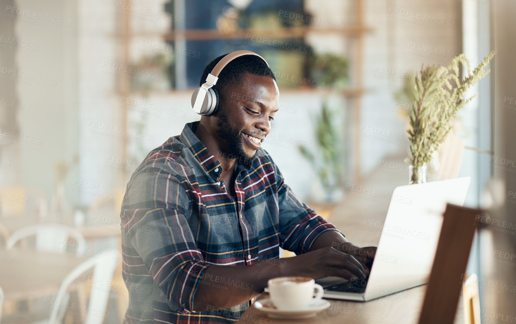 Buy stock photo Cropped shot of a handsome young businessman wearing headphones to listen to music and using his computer in a cafe