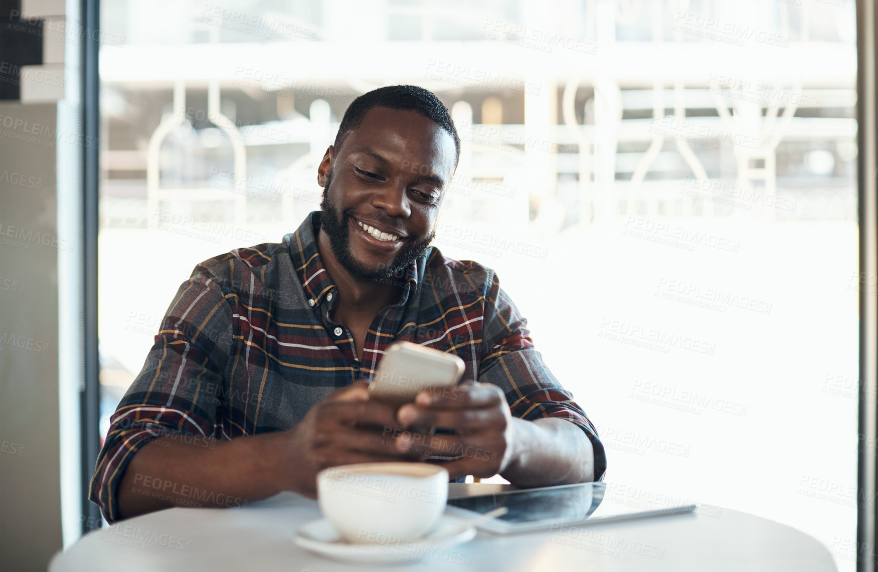 Buy stock photo Cropped shot of a handsome young businessman sitting alone in a cafe and using his cellphone