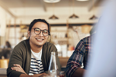 Buy stock photo Cropped shot of a handsome young man wearing spectacles and sitting with his friends in a coffee shop