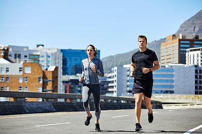 Buy stock photo Shot of two sporty young people out for a run in the city