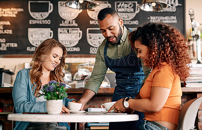 Buy stock photo Shot of a waiter serving two young women in a cafe