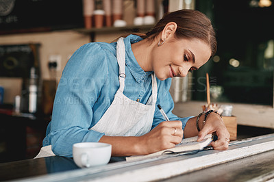 Buy stock photo Shot of a young woman writing notes while working in a cafe