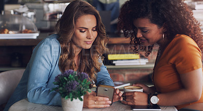 Buy stock photo Shot of two young women using a cellphone together in a cafe