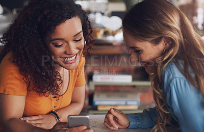 Buy stock photo Shot of two young women using a cellphone together in a cafe