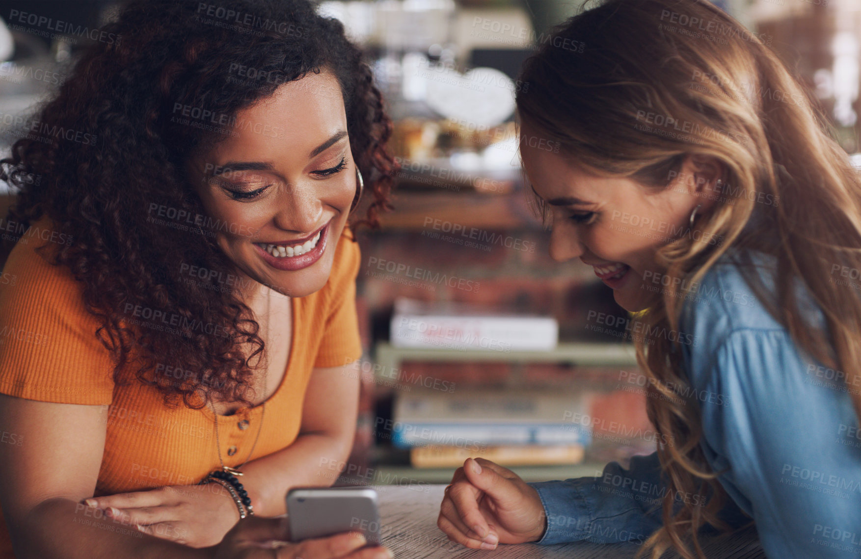 Buy stock photo Shot of two young women using a cellphone together in a cafe