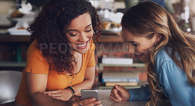 Buy stock photo Shot of two young women using a cellphone together in a cafe