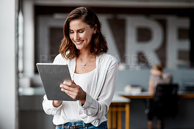 Buy stock photo Shot of an attractive young businesswoman standing alone in the office and using a digital tablet