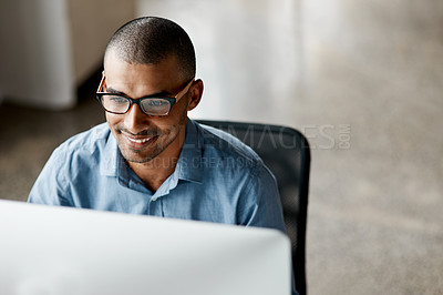 Buy stock photo Shot of a handsome young businessman sitting alone in the office and using his computer