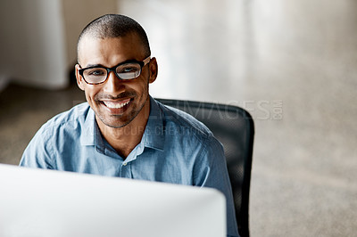 Buy stock photo Shot of a handsome young businessman sitting alone in the office and using his computer