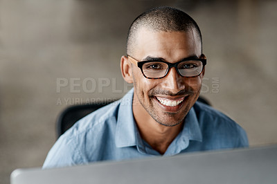 Buy stock photo Shot of a handsome young businessman sitting alone in the office and using his computer