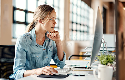 Buy stock photo Shot of an attractive young businesswoman sitting alone in the office and looking contemplative while using her computer