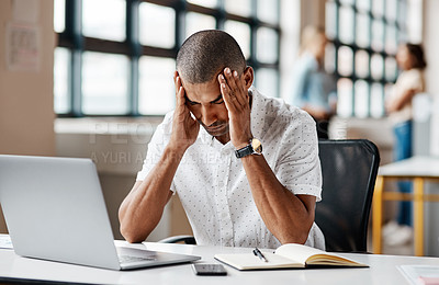 Buy stock photo Shot of a young businessman looking stressed out while working on a laptop in an office