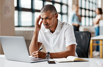 Buy stock photo Shot of a young businessman looking stressed out while working on a laptop in an office