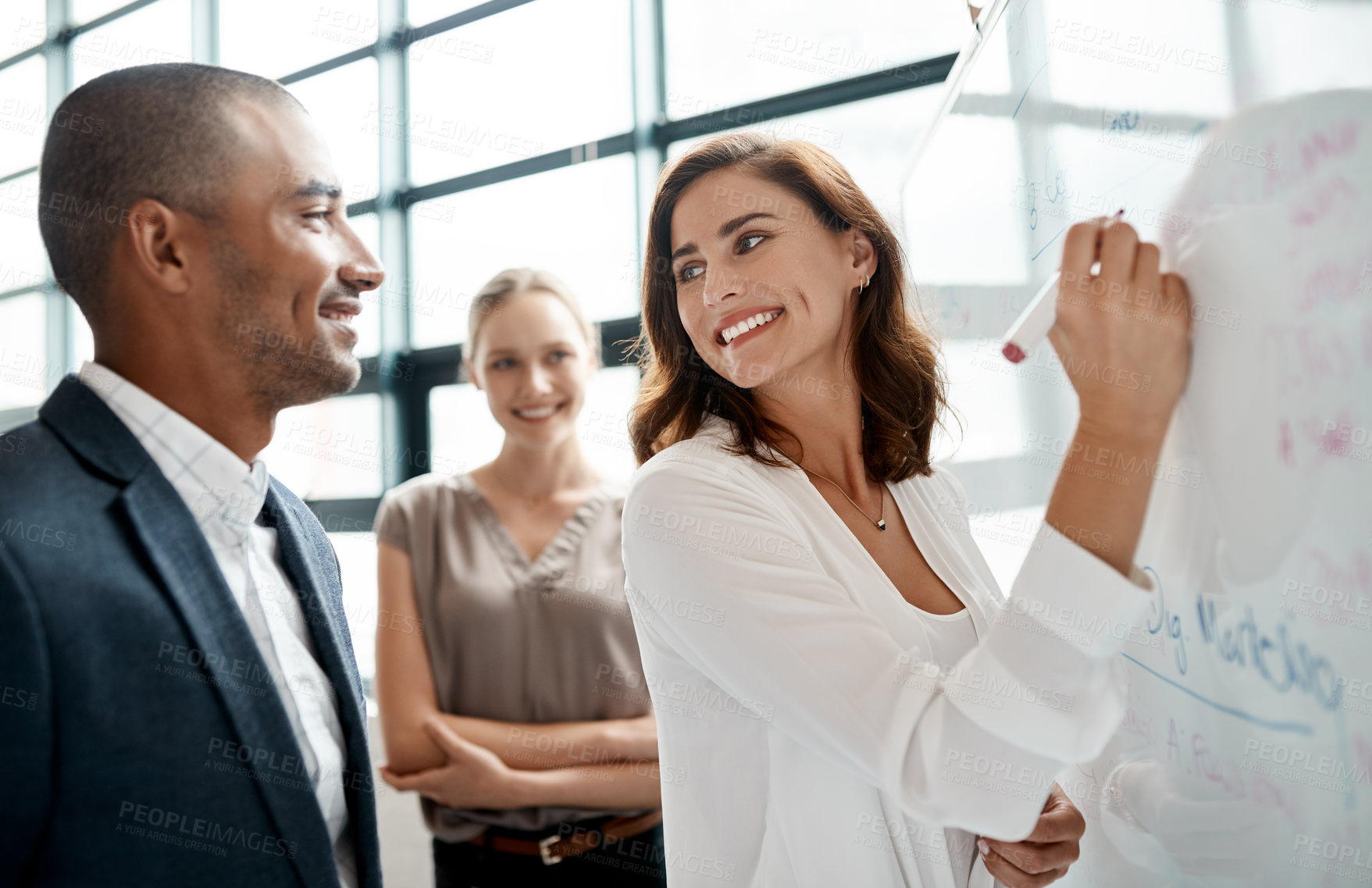 Buy stock photo Shot of a young businesswoman brainstorming on a whiteboard with her colleagues in an office