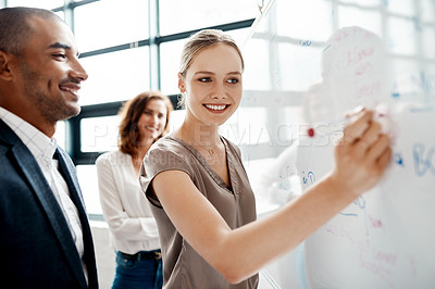 Buy stock photo Shot of a young businesswoman brainstorming on a whiteboard with her colleagues in an office