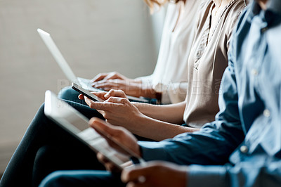 Buy stock photo Closeup shot of a group of unrecognisable businesspeople using digital devices while sitting in a row in an office