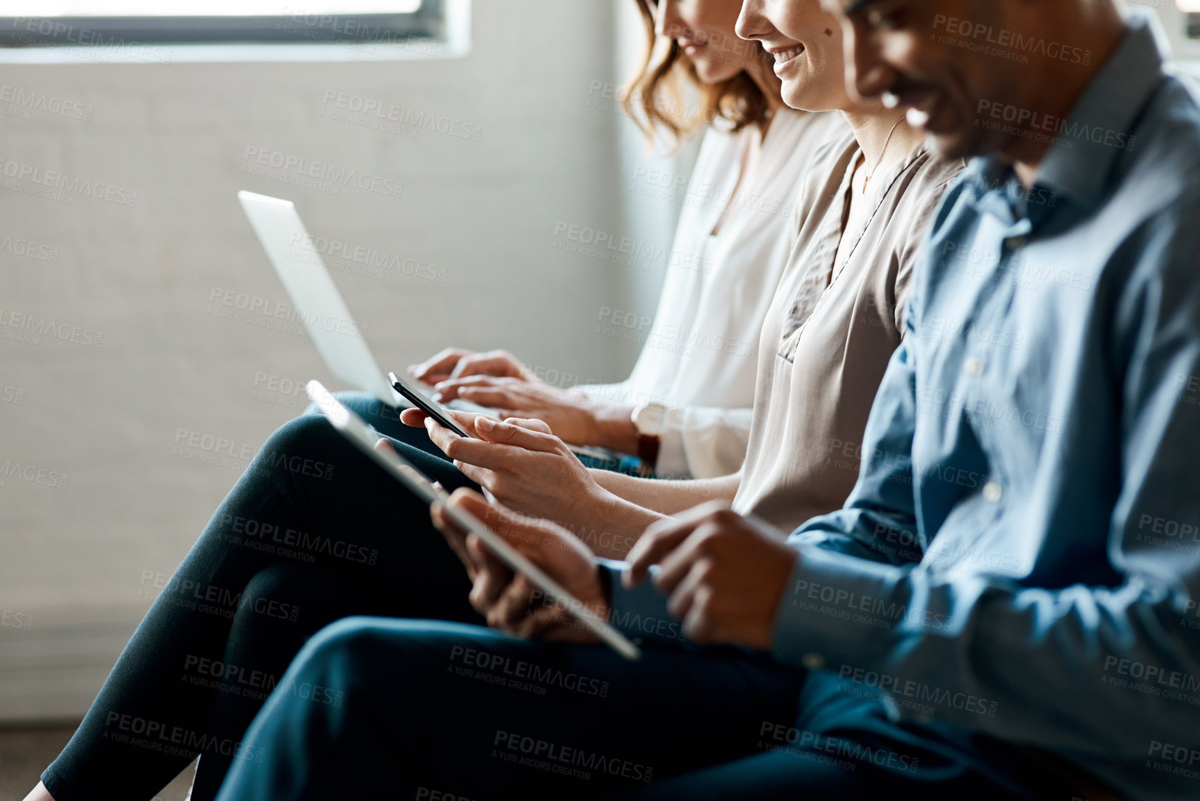 Buy stock photo Closeup shot of a group of unrecognisable businesspeople using digital devices while sitting in a row in an office