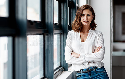 Buy stock photo Portrait of a confident young businesswoman standing at a window in an office
