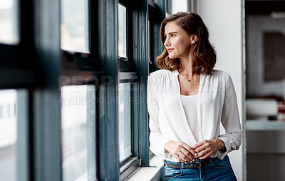 Buy stock photo Shot of a confident young businesswoman looking thoughtfully out a window in an office