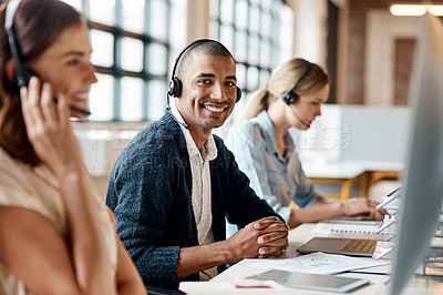 Buy stock photo Shot of a young man using a headset and computer in a modern office