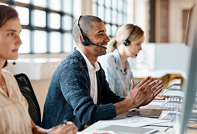 Buy stock photo Shot of a young man using a headset and computer in a modern office